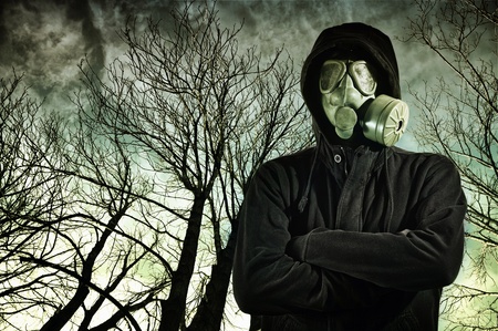 Man in dark clothes wearing a classic gas mask respirator, tree branches in the background.の写真素材