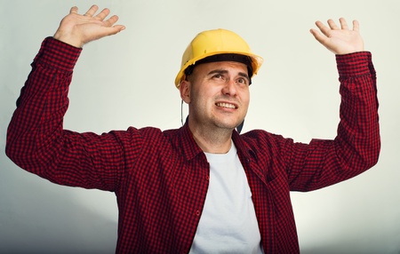 Construction worker in red shirt and yellow hardhat with raised handsの写真素材