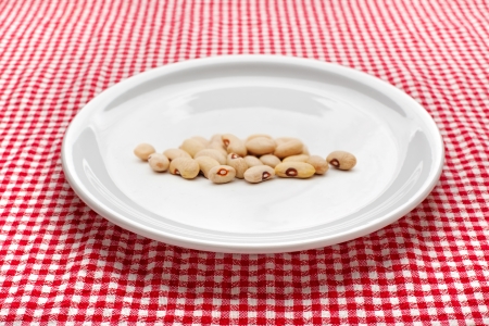 Raw kidney beans on white plate on kitchen table. Red and white checkered tablecloth in background.の写真素材