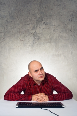 Bald yopung adult man sitting at the table with keyboard in front of the computerの写真素材
