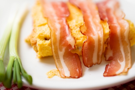 Bacon and scrambled eggs with green leek on white plate served as breakfast. Traditional breakfast with lots of calories.の写真素材