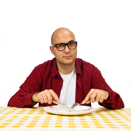 Young adult bold man sitting at the dinner table with fork and knife raised.の写真素材