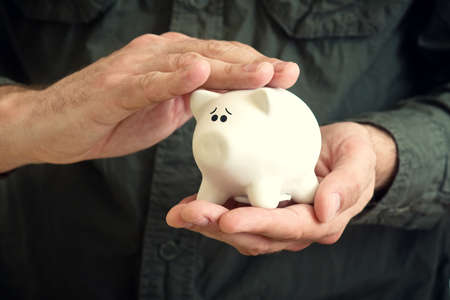 Hand cuddles white piggy coin bank with scared look in its eyes.の写真素材
