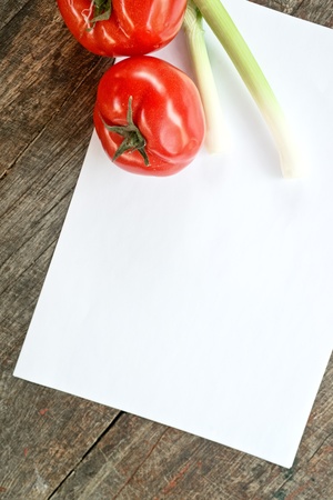 Tomato and spring onion on paper for recipe notes, on wooden table.の写真素材