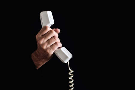 Hand holding white telephone receiver on dark background.の写真素材