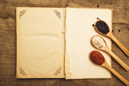 Spices. Food ingredients on wood spoons with open book on kitchen table.の写真素材