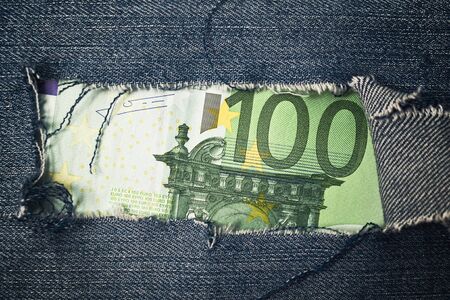 Hundred euros bill through torn blue jeans texture  European union economy concept の写真素材