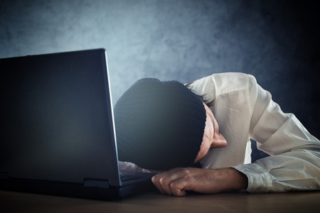 Exhausted man sleeps on laptop at office desk after working overtime.の写真素材