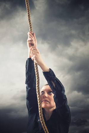 Woman climbing up with rope. Overcaming problems, obstacles and difficulties in life metaphor.の写真素材