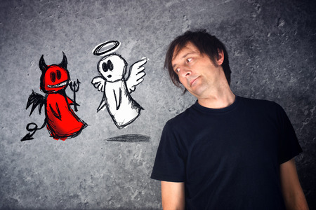 Casual man looking at doodle drawing of angel and devil fighting. Concept of conscience; decisions, uncertainty, moral dilemma; fight of good and evil.の写真素材