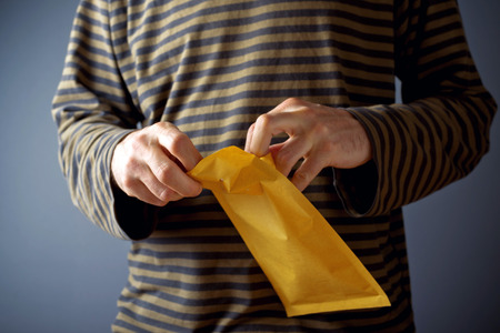 Casual man is opening yellow document postal envelopeの写真素材