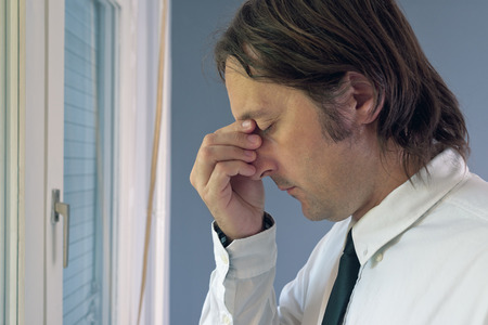 Businessman in trouble  Adult male standing by the office window having headache 