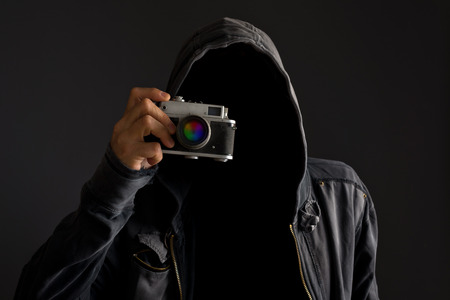 Faceless man with hoodie jacket holding dusty vintage film camera and taking photographs.の写真素材