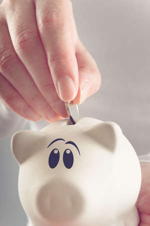 Woman putting coin in piggy coin bank, selective focus with shallow depth of field