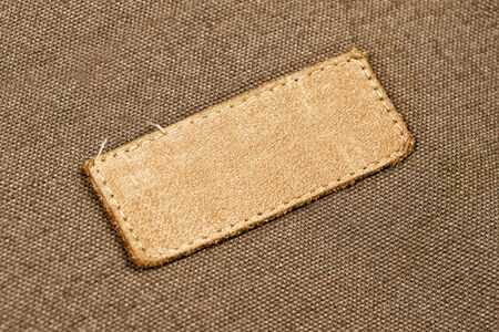 Blank Leather Label Tag on cotton fabric material texture background.