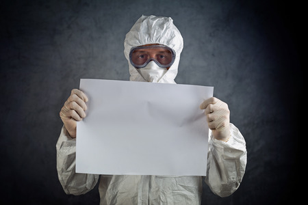 Medical healh care worker wearing protective gown, gloves, mask and goggles and holding blank paper...
