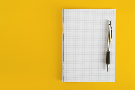 Ballpoint Pen and Blank Paper Notebook with as Business Copy Space on Yellow Background.