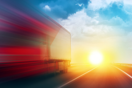 Speeding Transportation Delivery Truck on Open Highway with Sun Settimg Down on Horizon in Background. Speeding Transportation Delivery Truck on Open Highway with Sun Settimg Down on Horizon in Background.
