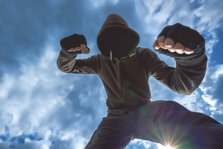 Violent attack, unrecognizable hooded male criminal kicking and punching victim on the street. Violent attack, unrecognizable hooded male criminal kicking and punching victim on the street.