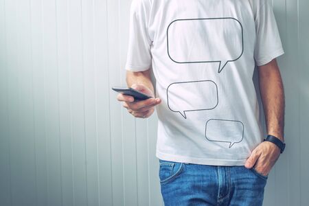 Guy with speech balloons printed on shirt using mobile phone to type and send text message