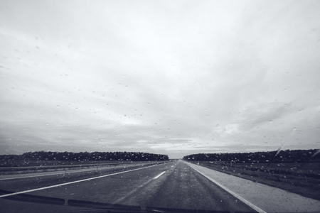 Raindrops on car windshield glass, monochromatic image of open highway through vehicle windscreen on a rainy dayの写真素材