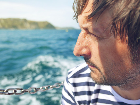 Bearded pensive male looking at the sea from yacht, thoughtful successful adult sailor on bright sunny summer day enjoying vacation holidaysの写真素材