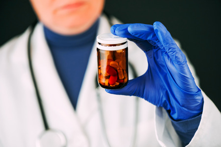 Female doctor holding unlabeled bottle of various pills and medication, prescription medicine and healthcare, selective focusの写真素材