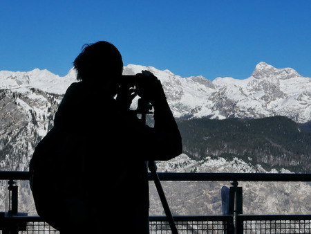 Silhouette of male landscape photographer capturing breathtaking view of snow capped mountain rangeの写真素材