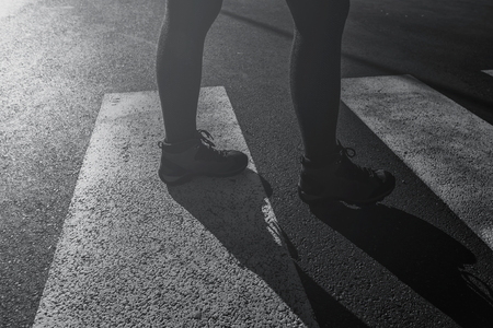 Woman walking on street over pedestrian zebra crossing, backlit female legs wearing hiking boots in urban surroundingsの写真素材