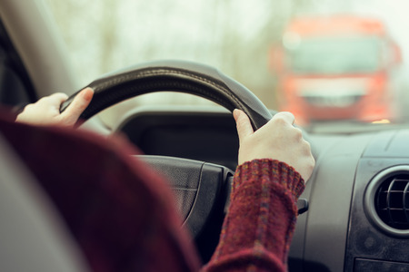 Woman driving car toward a large truck on the road, selective focus on hands gripping the steering wheel of the vehicle, retro toned imageの写真素材