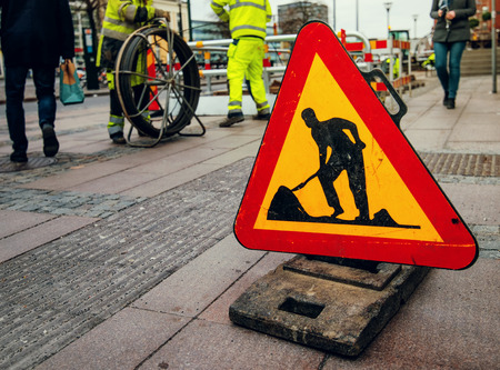 Road works sign on city street, workers and pedestrians in the backgroundの写真素材