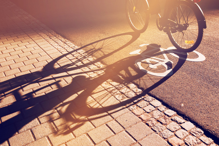 Shadow of unrecognizable cyclist riding a bike on bicycle lane through city street next to the road marking in urban surrounding, retro tonedの写真素材