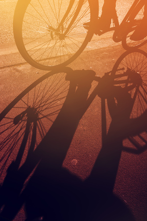 Shadow of unrecognizable cyclist riding a bike on road through city street in urban surrounding, retro tonedの写真素材