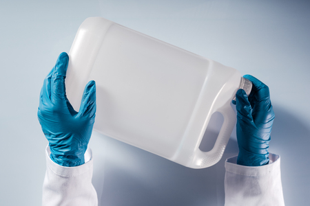 Chemical scientist opening white unlabeled plastic tank canister with chemicals on laboratory table
