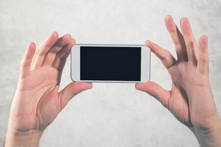 Male hand holding mobile phone with blank mock up screen as copy space, man using modern white smart...