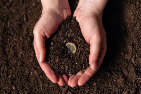 Making income from agricultural activity and earning extra money, female farmer handful of soil with euro coinの写真素材