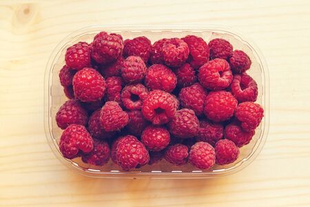 Top view of ripe raspberries in plastic container box on wooden table, retro toned imageの写真素材