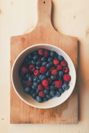 Raspberries and blueberries in bowl, top viewの写真素材