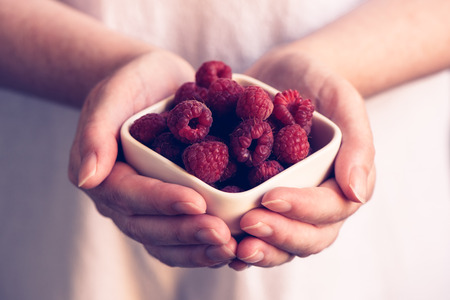 Woman offering a bowl of raspberries, selective focus