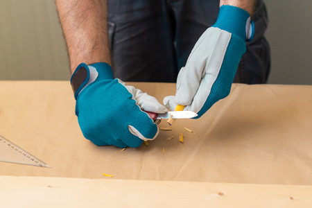 Carpenter handyman sharpening pencil with pocket knife on woodwork workshop table, selective focus