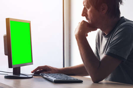 Freelancer working on home office desktop PC computer. Monitor has green screen as mock up copy...