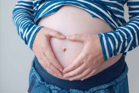 Pregnant woman touching and rubbing her belly, mother stroking and stimulating abdomen, adult caucasian female in fifth month or twenty first week of pregnancy (second trimester)の写真素材