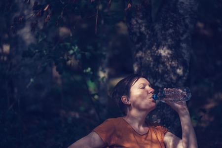 Woman drinking water outdoors. Thirsty adult caucasian female refreshing after long walk through...