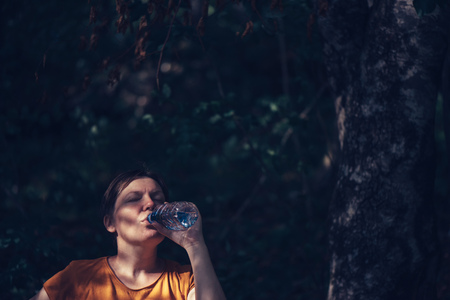 Woman drinking water outdoors. Thirsty adult caucasian female refreshing after long walk through...