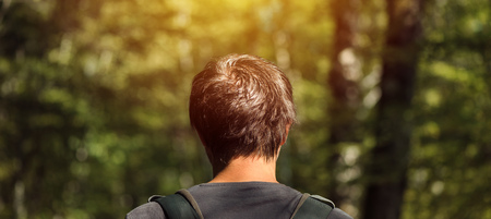 Rear view of adult caucasian male with backpack enjoying a walk in the park on sunny summer afternoon. Healthy lifestyle, recreation and nature loving concept.の写真素材