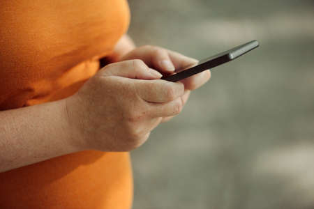 Pregnant woman texting outdoors on park bench, adult caucasian female using mobile phone during pregnancyの写真素材