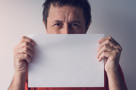 Man hiding behind blank white paper as copy space for text messageの写真素材