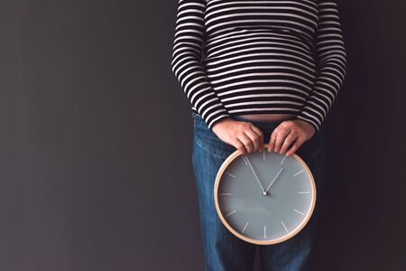 Pregnant female with vintage alarm clock expecting baby in third trimester of pregnancyの写真素材