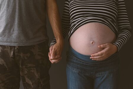 Soldier and his pregnant wife holding hands, couple expecting baby, low keyの写真素材