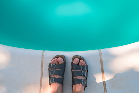 Bare male feet in slippers by the poolside. Barefoot man standing, relaxing and chilling out by the swimming pool.の写真素材
